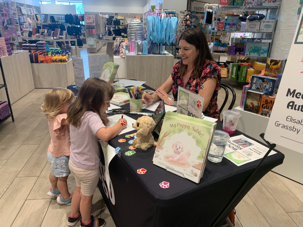 Two children colouring on colouring paper and talking to Liz at her book signing.