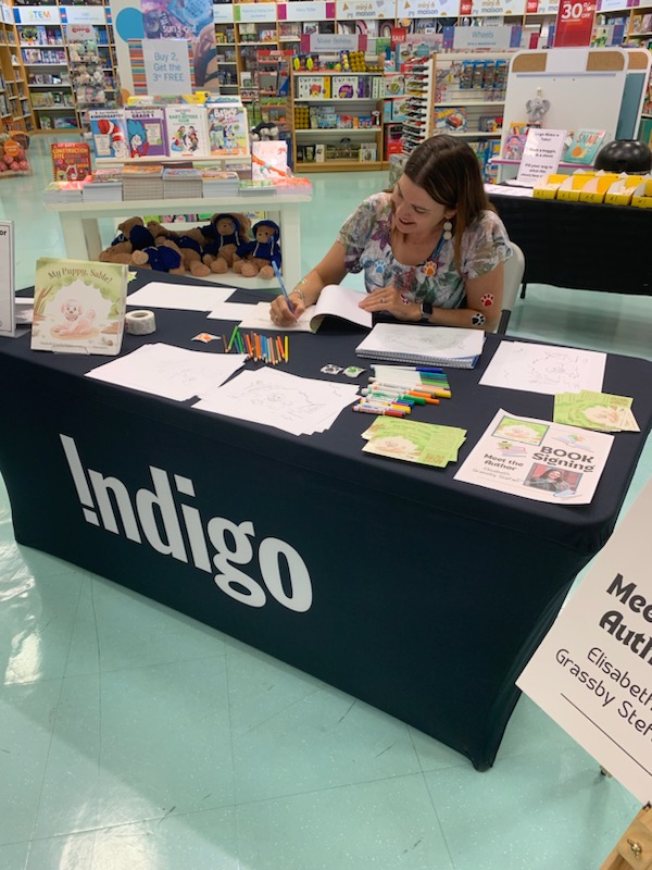 Liz signing books with coloured pencils at a table at Indigo.